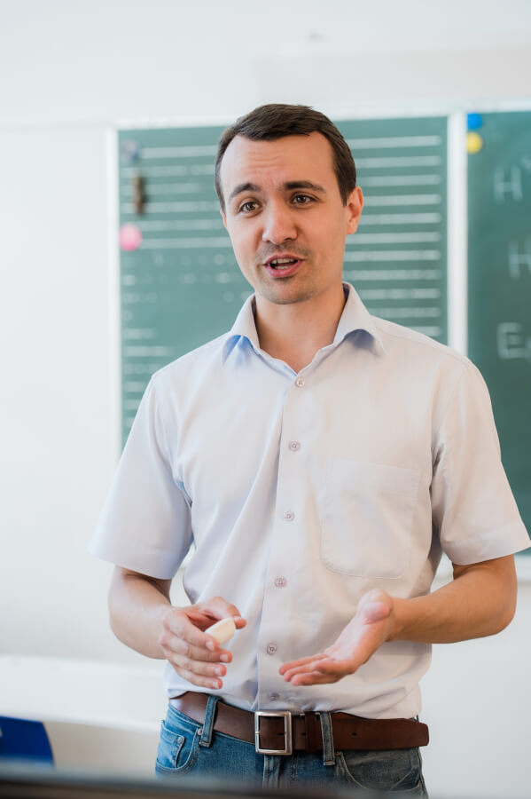 Young teacher near chalkboard in school classroom talking to class